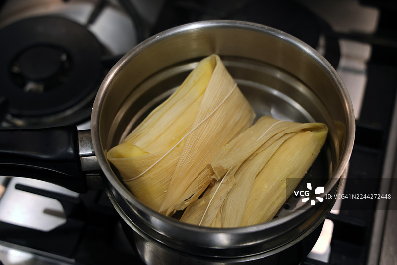 蒸锅里的两个奶酪番石榴馅玉米饼（一种哥伦比亚传统玉米饼，内填奶酪和番石榴酱，用玉米叶包裹烹制）放在燃气灶上图片素材