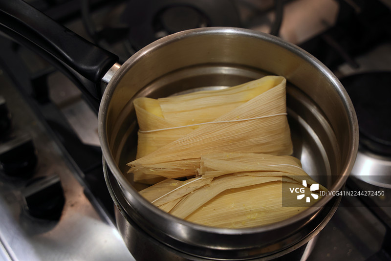 两个用玉米叶包裹的奶酪番石榴馅玉米饼（哥伦比亚传统玉米饼，内馅为奶酪和番石榴酱，用玉米叶包裹后烹制）放在燃气灶的蒸锅里图片素材