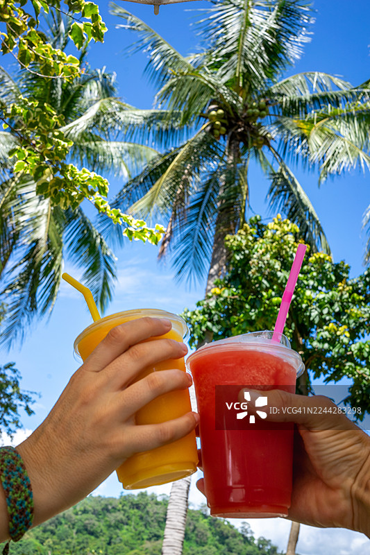 在棕榈树下，举杯畅饮清爽的果昔，庆祝热带假期，享受夏日度假和天堂般的健康生活方式图片素材