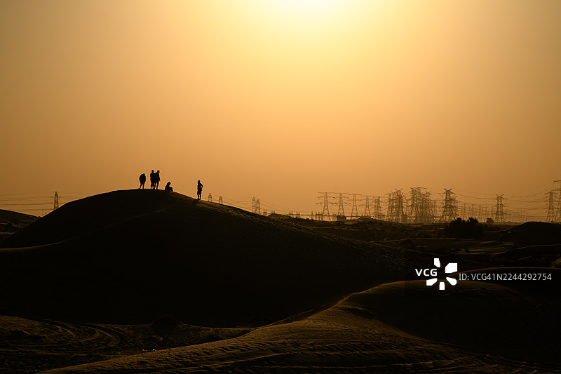日落时分，迪拜阿联酋，沙丘上五人剪影，远处有电力线图片素材
