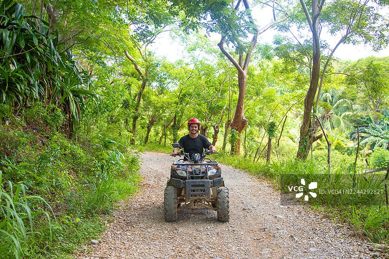 一位戴着安全头盔的男人微笑着，在洪都拉斯罗阿坦的一条土路上驾驶着一辆全地形车图片素材