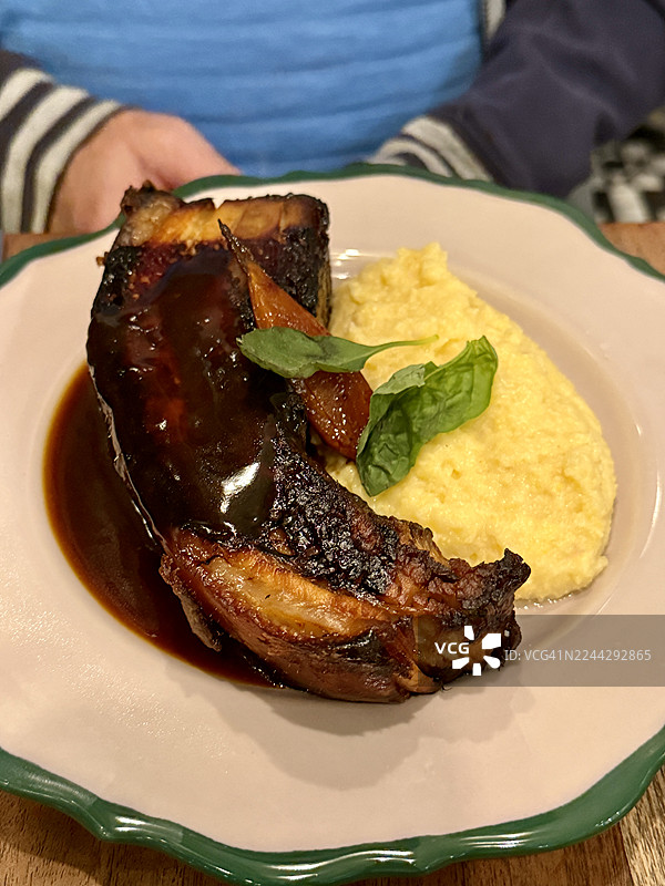 特写：一个男人坐在桌前，桌上摆着烤猪肚、玉米糊和酱汁的盘子图片素材