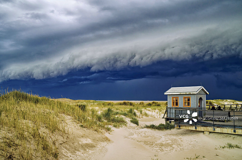 德国石勒苏益格-荷尔斯泰因州北弗里斯兰区圣彼得奥尔丁的沙滩上，一座木制海滩小屋在戏剧性的风暴之下图片素材
