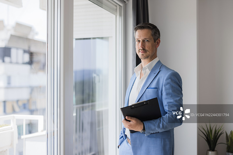自信的商人在窗边拿着文件夹图片素材
