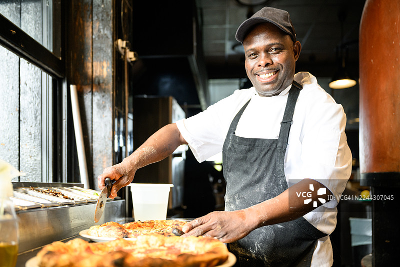 一位快乐的专业厨师在现代餐厅厨房的柜台前准备新鲜披萨的肖像图片素材