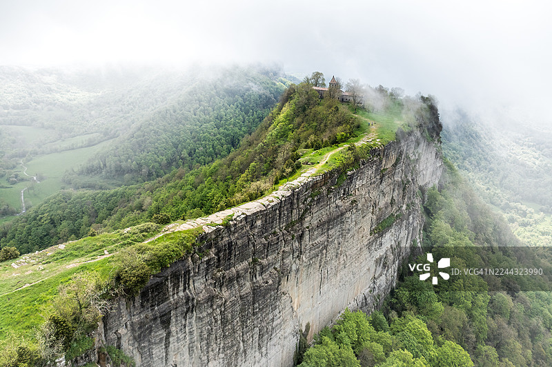 卡夫雷拉圣殿坐落于陡峭的山崖之上，俯瞰着被茂密森林覆盖的广阔绿色山谷，薄雾温柔地笼罩着这片高耸的土地。图片素材