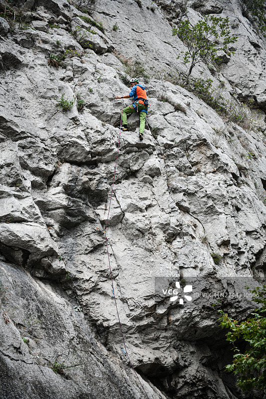 佩戴头盔、安全带和绳索的登山者在户外攀岩探险中，在陡峭的岩壁上休息图片素材