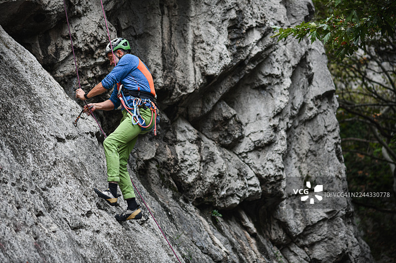 身系安全装备、头戴绿色头盔、使用紫色绳索的攀岩者悬挂在岩壁上进行户外探险图片素材