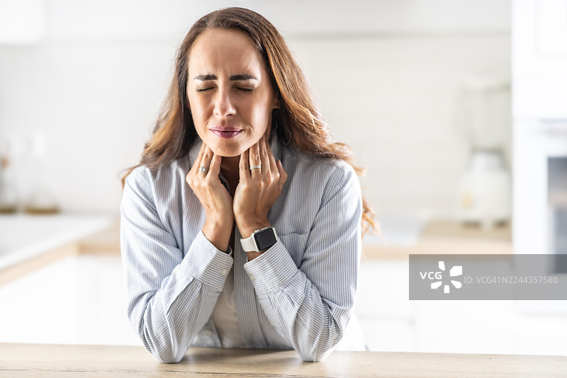年轻女子揉着发炎的扁桃体，扁桃体炎问题，已裁剪。女子有甲状腺问题，触摸着脖子，女孩喉咙痛。图片素材