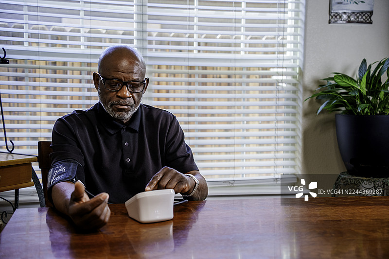 一位年迈的男士在家中使用自动化设备测量血压图片素材