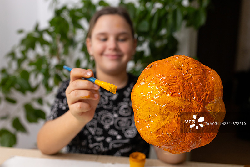 一个人微笑着，用彩色的画笔为万圣节纸浆南瓜上色图片素材