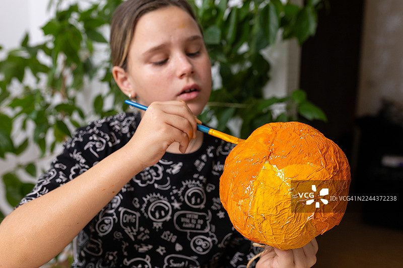 小女孩在万圣节手工课上绘制一个亮橙色的纸浆南瓜图片素材