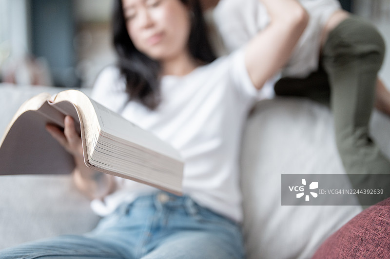 亚洲女性在沙发上读书，孩子在旁边，温馨的家庭居家时光图片素材