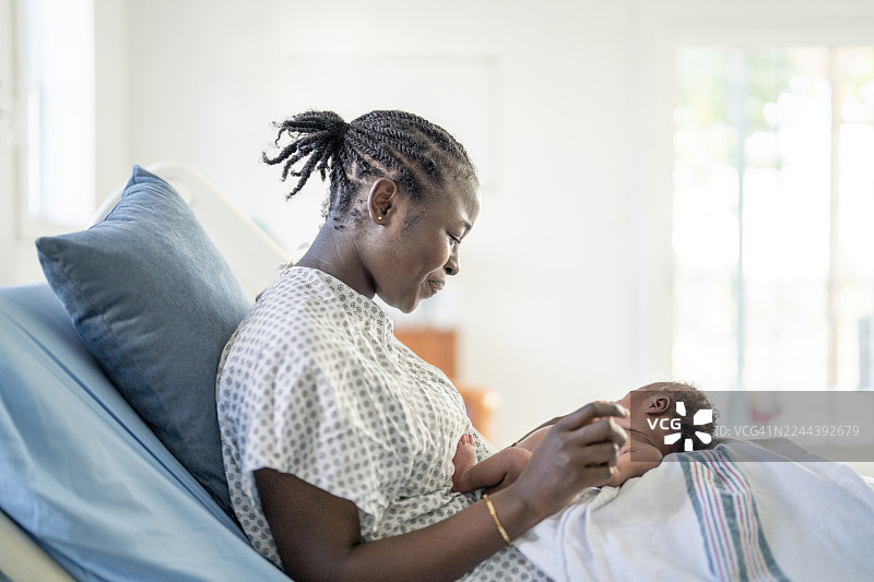在家医院病床上哺乳新生儿的黑人母亲，分娩后温馨的家庭时刻，喜悦的亲子联结图片素材
