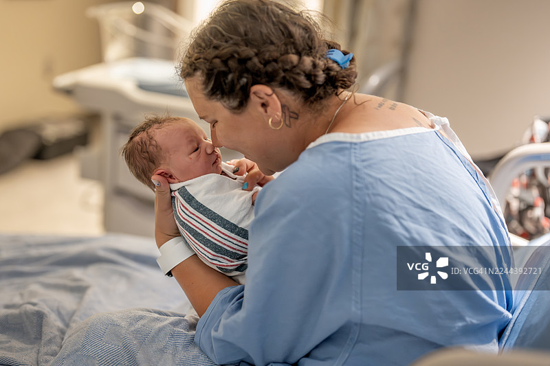 母亲在产后抱着新生儿躺在医院病床上，温馨的时刻图片素材