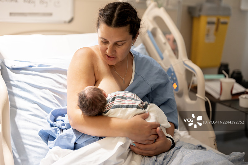 新生儿出生后，新妈妈在医院病床上轻柔地抱着新生儿——温馨的家庭时刻图片素材