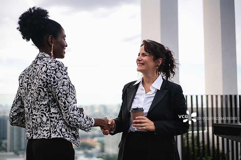 两位女商人正在摩天大楼的屋顶上握手表示祝贺图片素材