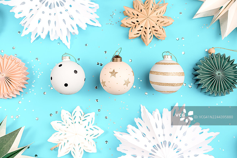 蓝色背景上节日氛围的纸雪花和圣诞装饰品组成的构图。圣诞快乐，新年快乐的概念图案。图片素材