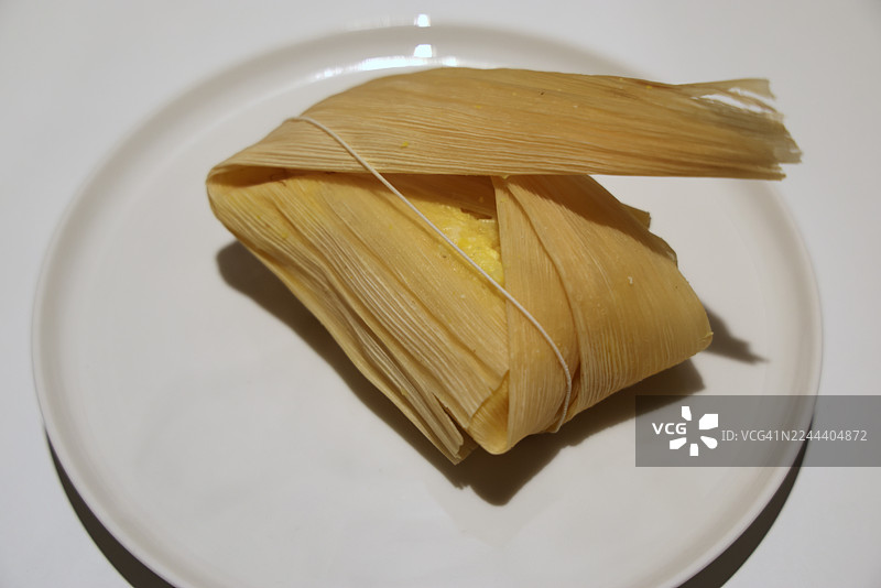 用玉米叶包裹、用玉米叶蒸煮的，内含奶酪和番石榴酱的哥伦比亚传统玉米蛋糕（奶酪番石榴蛋糕）放在盘子里图片素材