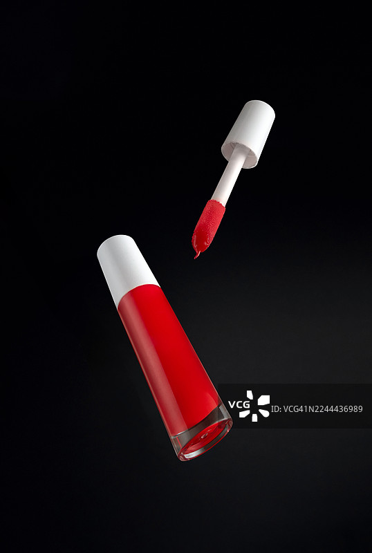 带有蓬松刷子的亮红色唇彩瓶，背景为深色图片素材
