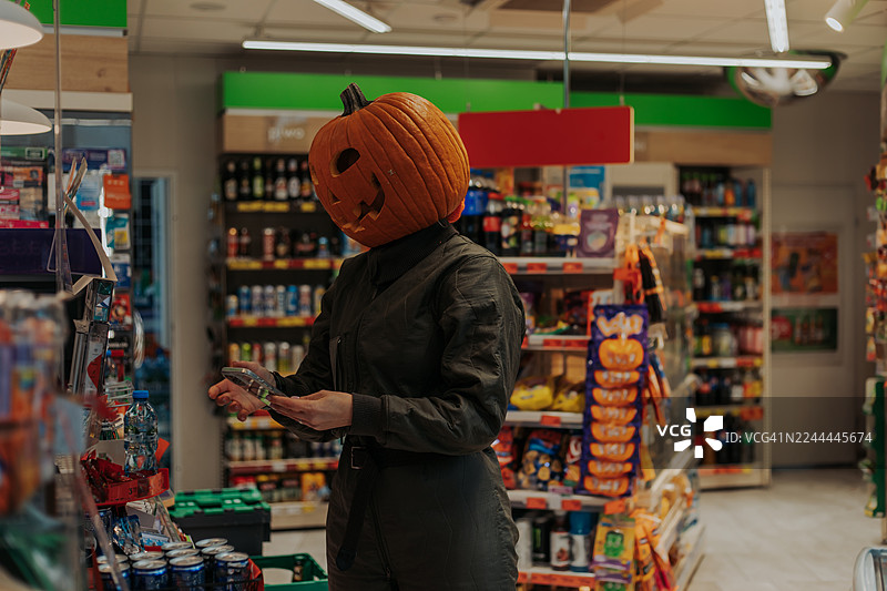 万圣节顾客戴着南瓜头服装在便利店过道浏览图片素材