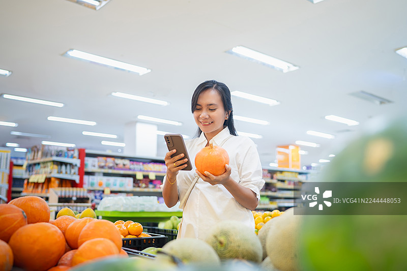 女士在标签和手机上比较南瓜价格图片素材