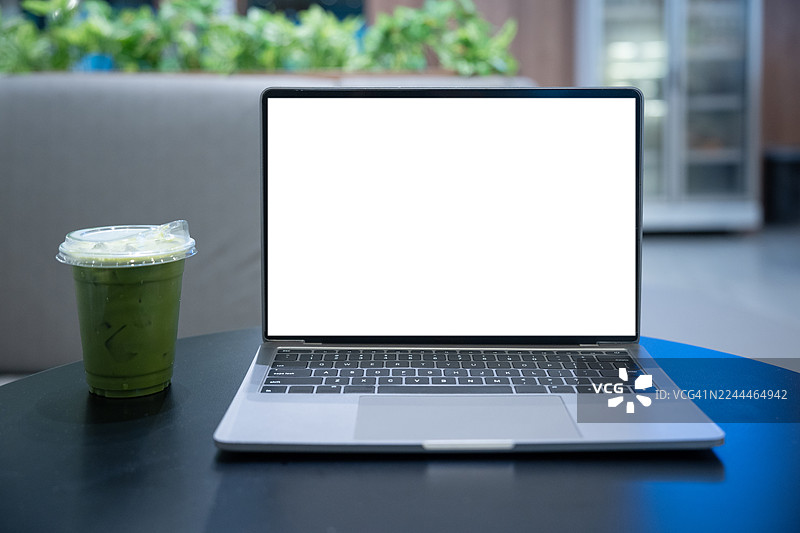 咖啡馆背景的桌子上放着一台屏幕空白的笔记本电脑。笔记本电脑屏幕带有复制空间。舒适的工作场所。正面视图。网上冲浪。视频会议。在线购物。图片素材