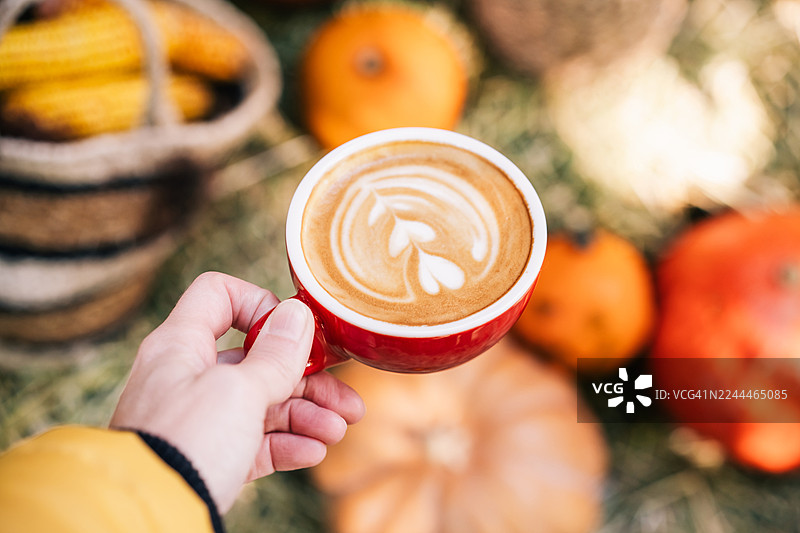 阳光明媚的秋日，卡布奇诺咖啡上有着拉花艺术，背景点缀着南瓜。图片素材