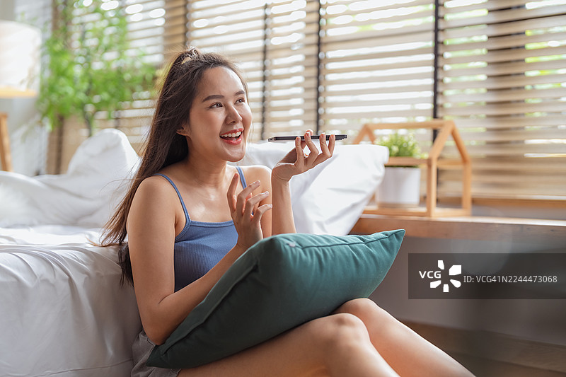 一位美丽、知性休闲的亚洲女性自信地使用智能手机，在人工智能的协助下，获得智能回复，并规划她的周末旅行。图片素材