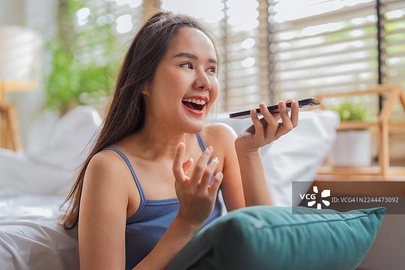 一位美丽、知性休闲的亚洲女性自信地使用智能手机，在人工智能的协助下获得智能回复，并规划她的周末旅行。图片素材