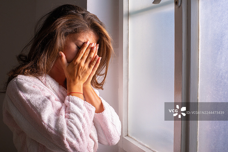 患有癌症的年轻女子穿着浴袍，透过医院窗户向外看图片素材