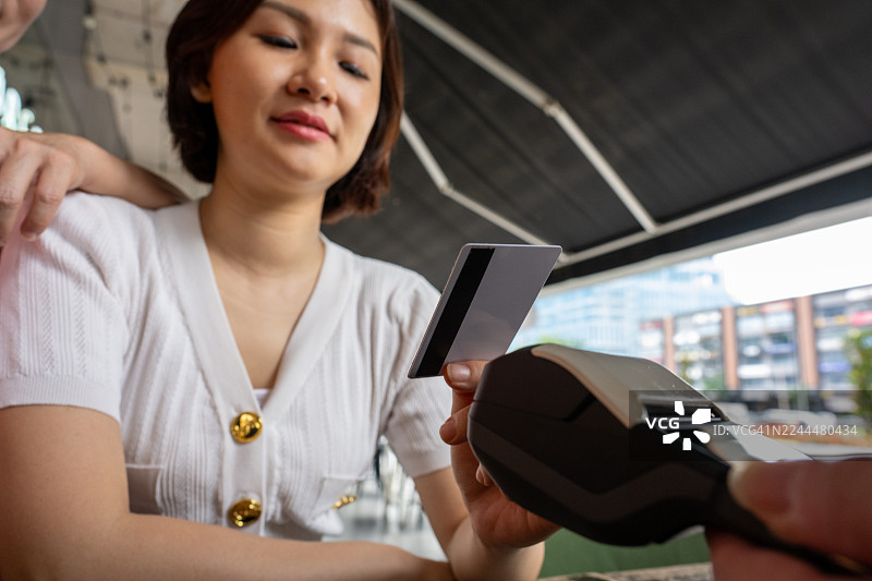 一位亚洲女性在咖啡馆用电子读卡器刷信用卡支付。图片素材