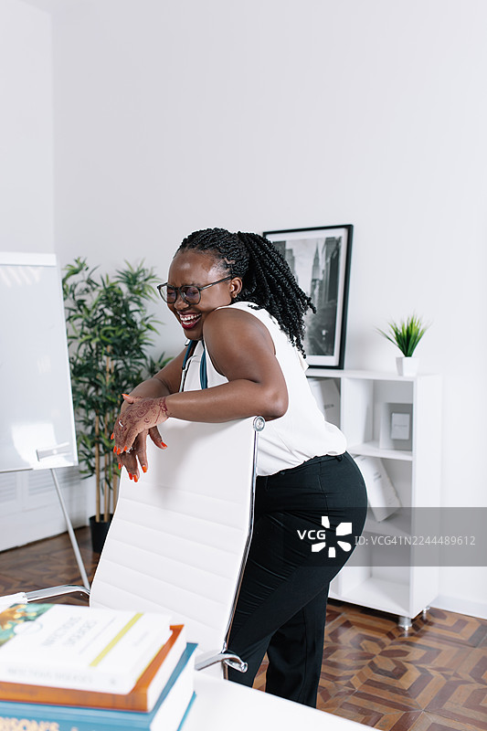 快乐的医务工作者倚靠在白色椅子上，在明亮现代的办公空间里，面带微笑，神情放松图片素材