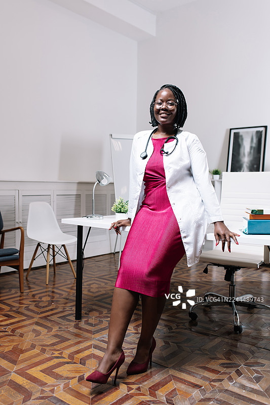 自信的女医生身穿粉色连衣裙和白大褂，站在现代化的诊室里图片素材