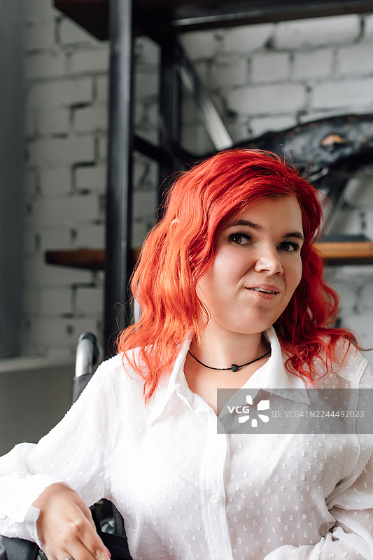 一位身穿白色女衬衫、留着一头亮红色头发的女性肖像，置身于休闲的室内环境图片素材