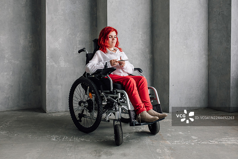 一位坐在轮椅上的女性在现代混凝土空间、都市室内使用智能手机图片素材