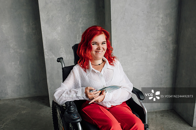 一位自信的女士坐在轮椅上，在现代室内环境中阅读手册时面带微笑图片素材