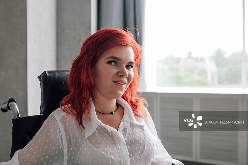 一位自信的红发女子坐在轮椅上，身处现代办公室的肖像照图片素材