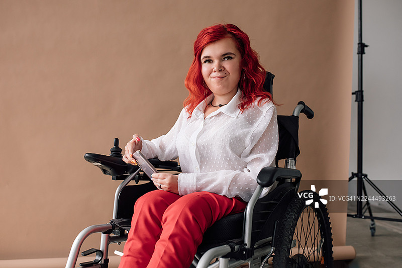 工作室里，一位坐在轮椅上的快乐女士正拿着一个设备，拍摄肖像照图片素材