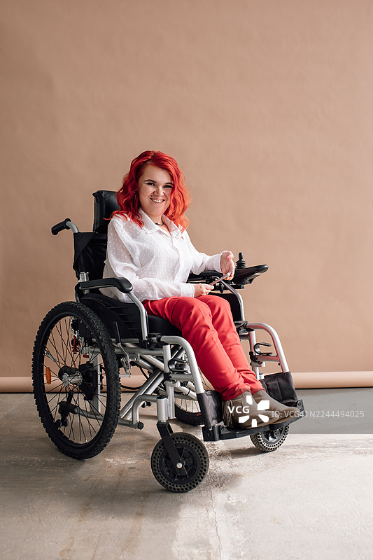 坐着轮椅的快乐红发女子，身穿休闲服饰，在影棚中微笑的肖像照图片素材