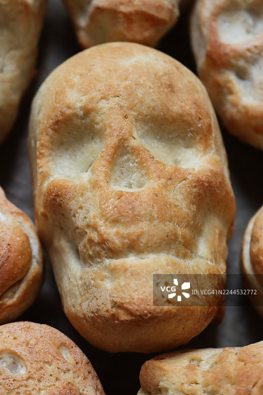 全画幅图像，展示烤盘上铺着烘焙纸，上面放着自制的、刚出炉的、骷髅形状的面包卷，俯视角度，万圣节家庭烘焙概念图片素材