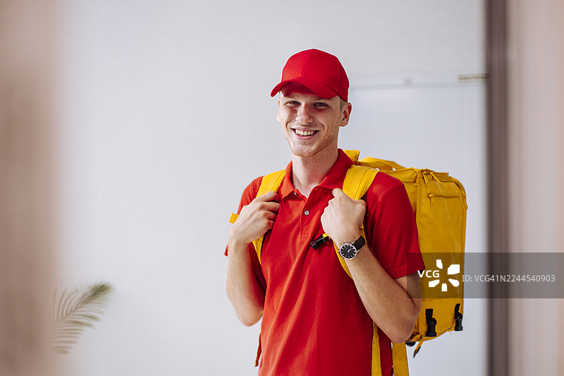 Smiling Delivery Person in Red Uniform With Yellow Backpack Ready for Work图片素材