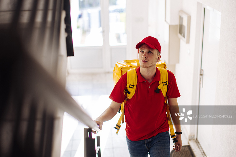 身着红色制服、背着黄色背包的配送员进入大堂递送包裹图片素材