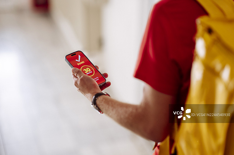 身穿红衣、背着黄背包的旅行者今天在走廊里用智能手机查看手机应用程序图片素材