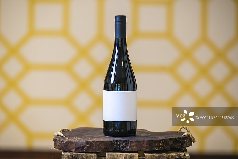 黄色背景下，木制底座上的单一酒瓶。图片素材