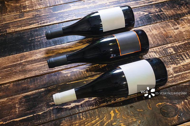 三瓶葡萄酒倒在质朴的木桌上。图片素材