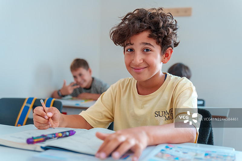 小学生在教室里坐着，手里拿着笔，脸上带着微笑图片素材