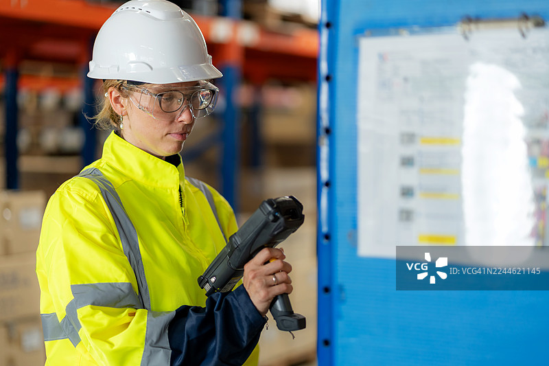 一名身穿安全装备的仓库员工在发货前使用条形码扫描仪扫描产品箱。体现了利用智能技术进行的货物运输、库存控制、物流准确性、供应链管理和工业效率的概念。图片素材