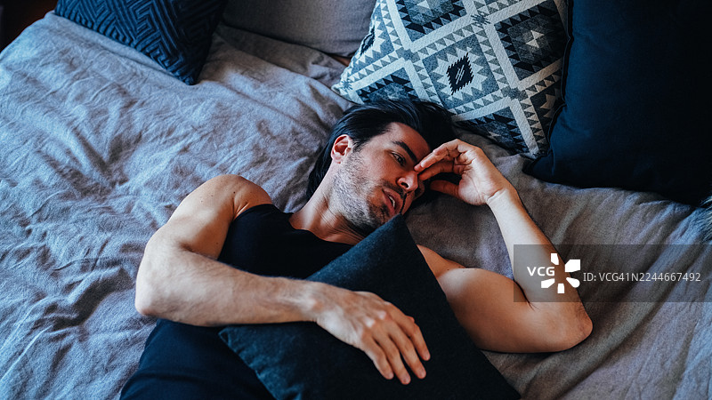 沮丧的男人躺在床上，抱着枕头。图片素材