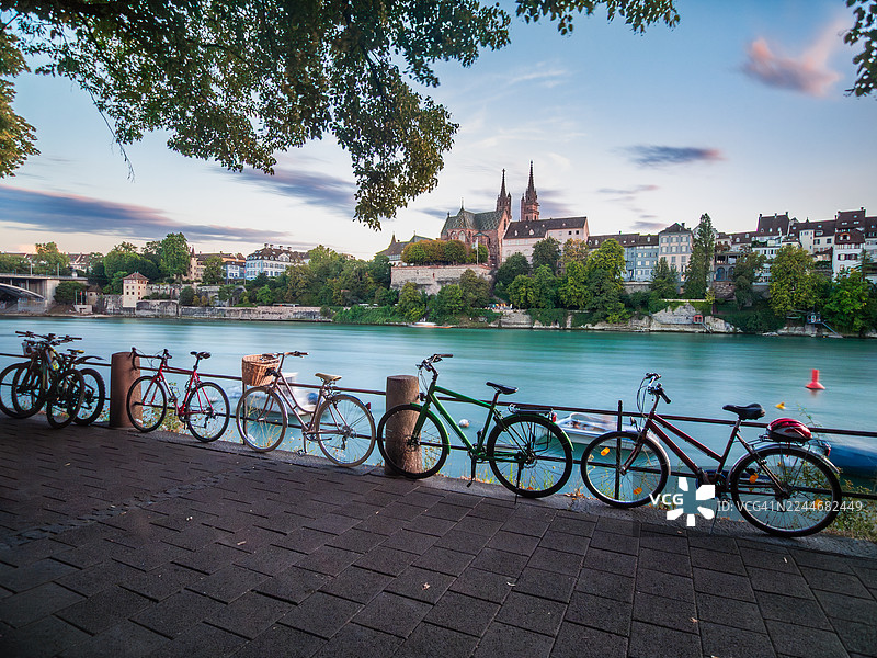 瑞士巴塞尔，巴塞尔城市地区，老城区莱茵河畔长廊的慢门长曝光景观，黄昏时分，可以看到一排自行车、船只，以及巴塞尔大教堂和美丽的巴洛克式建筑的视角。图片素材